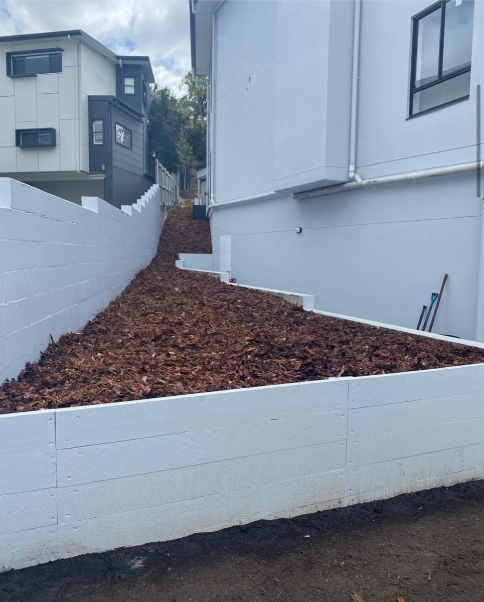 Finished white timber retaining wall with fresh mulch on a sloped block
